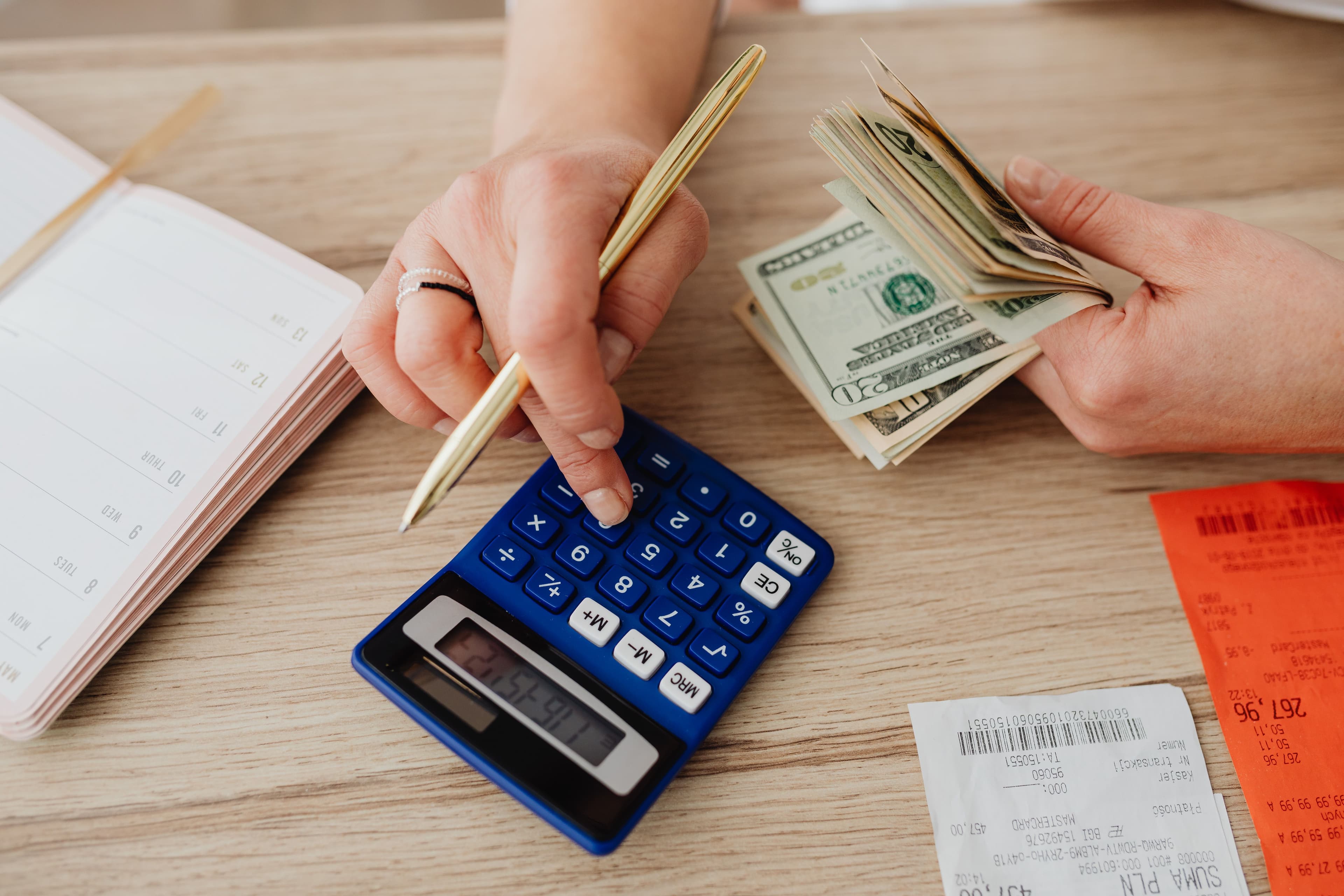 Hands using a calculator and counting cash beside receipts