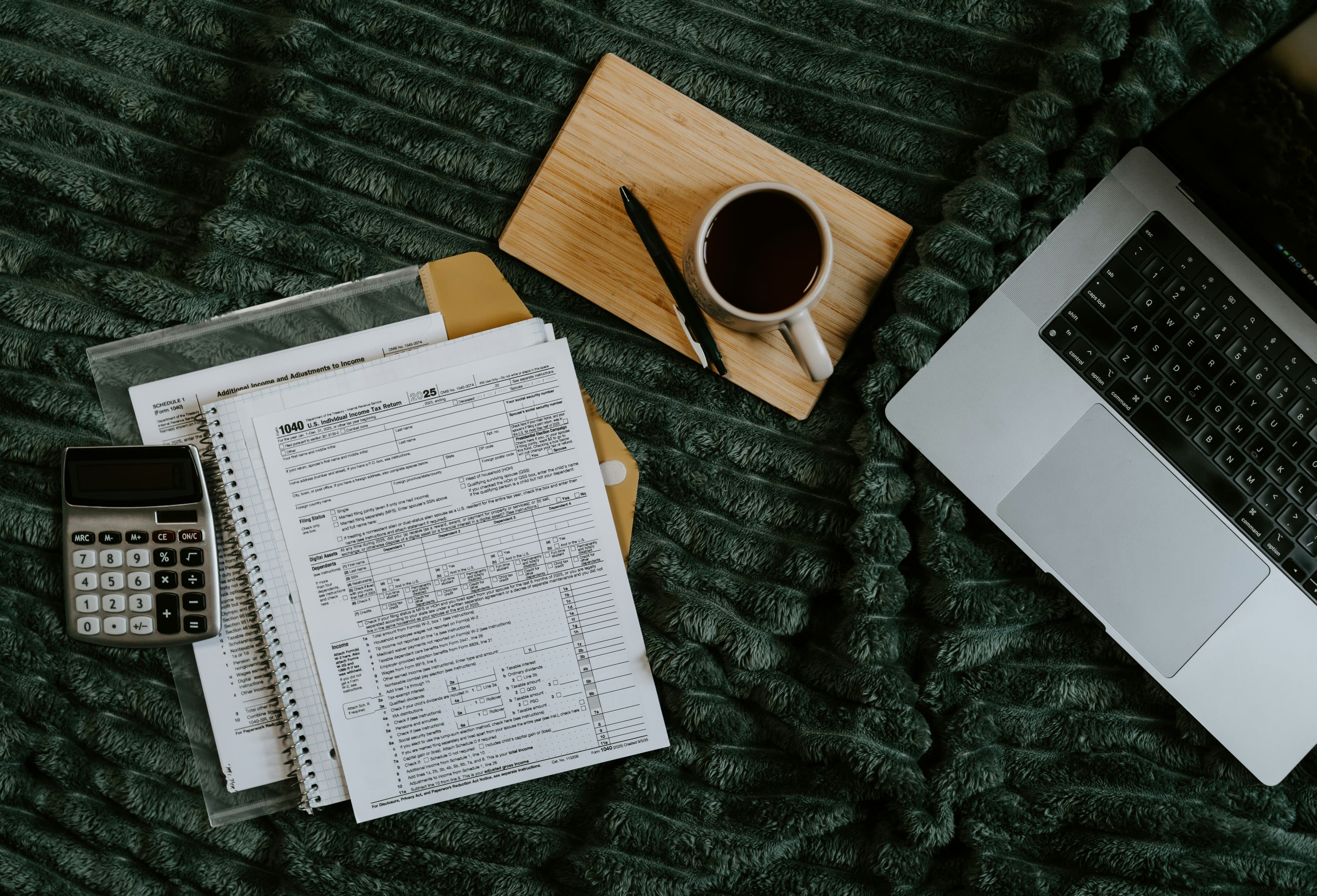 A 1040 tax form, calculator, and laptop laid out on a blanket