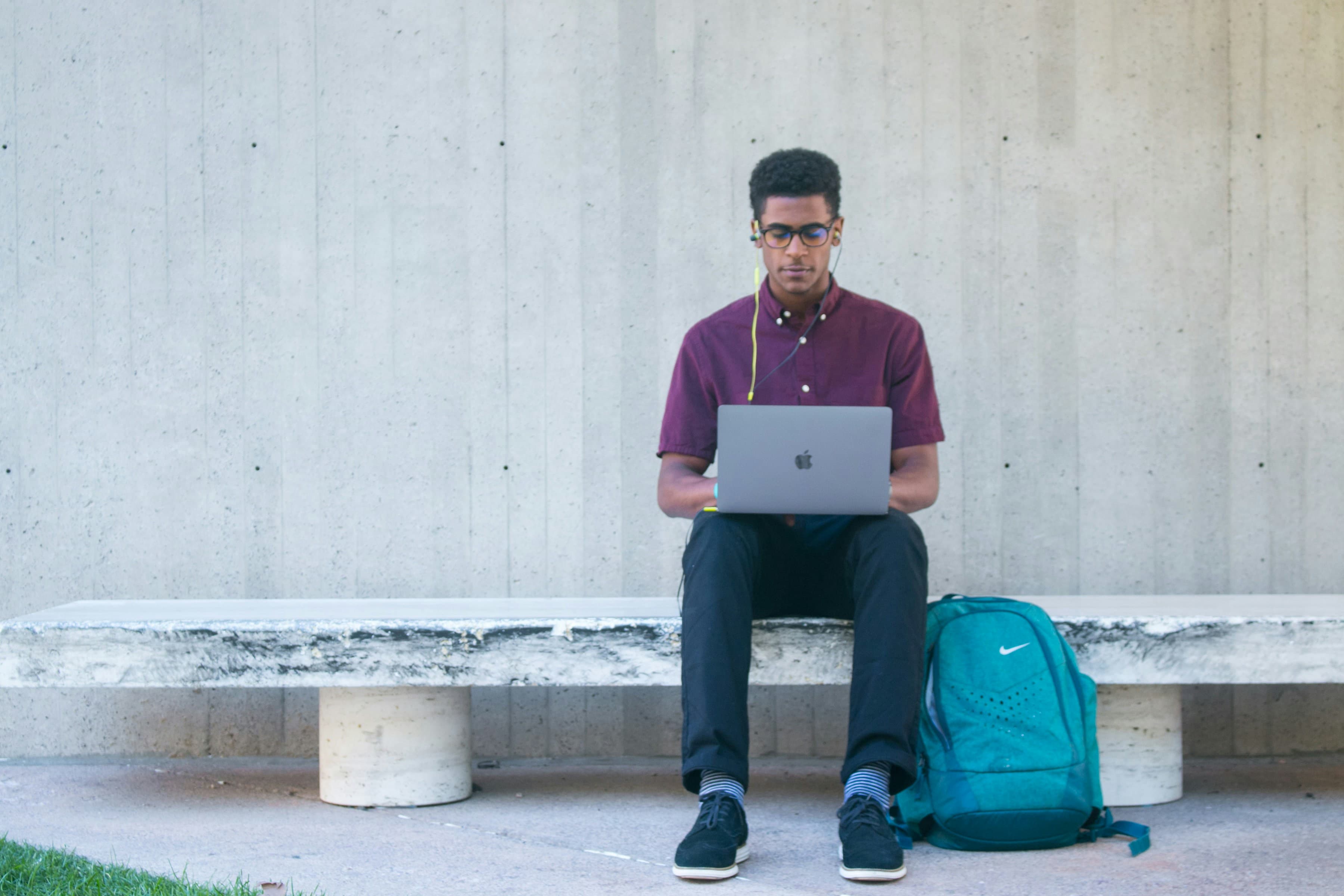 A student using a laptop on a campus bench with a backpack