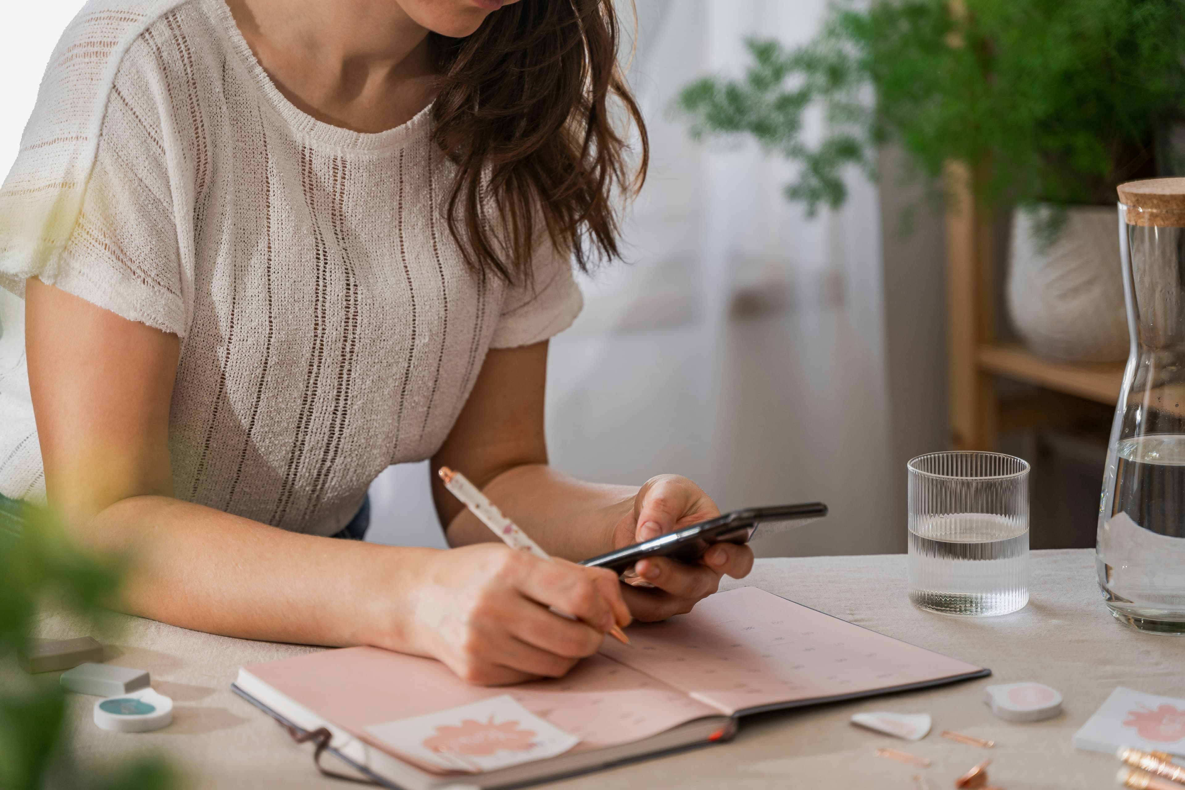 A young woman writing in a planner while holding her phone