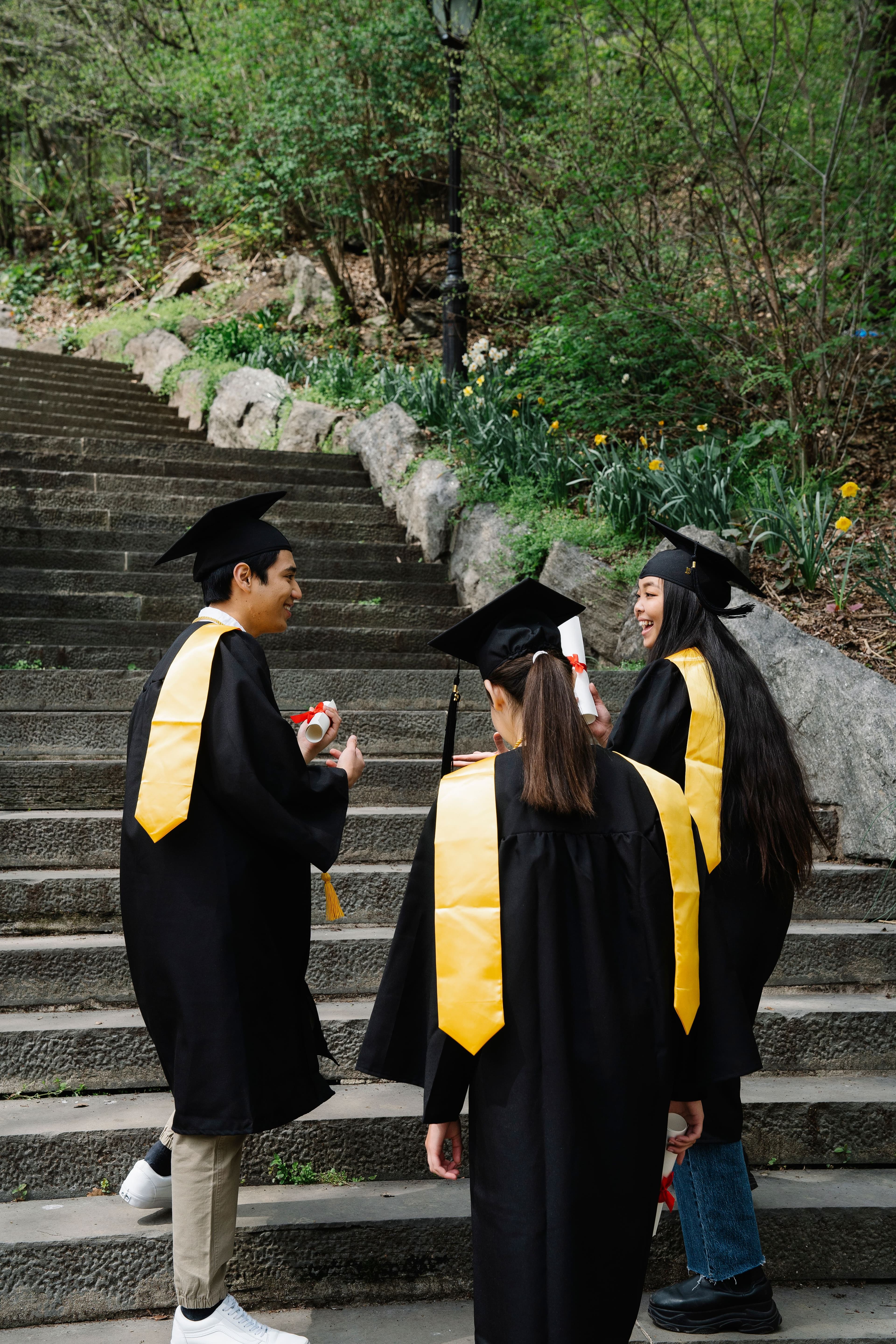 Three young graduates in caps and gowns holding their diplomas