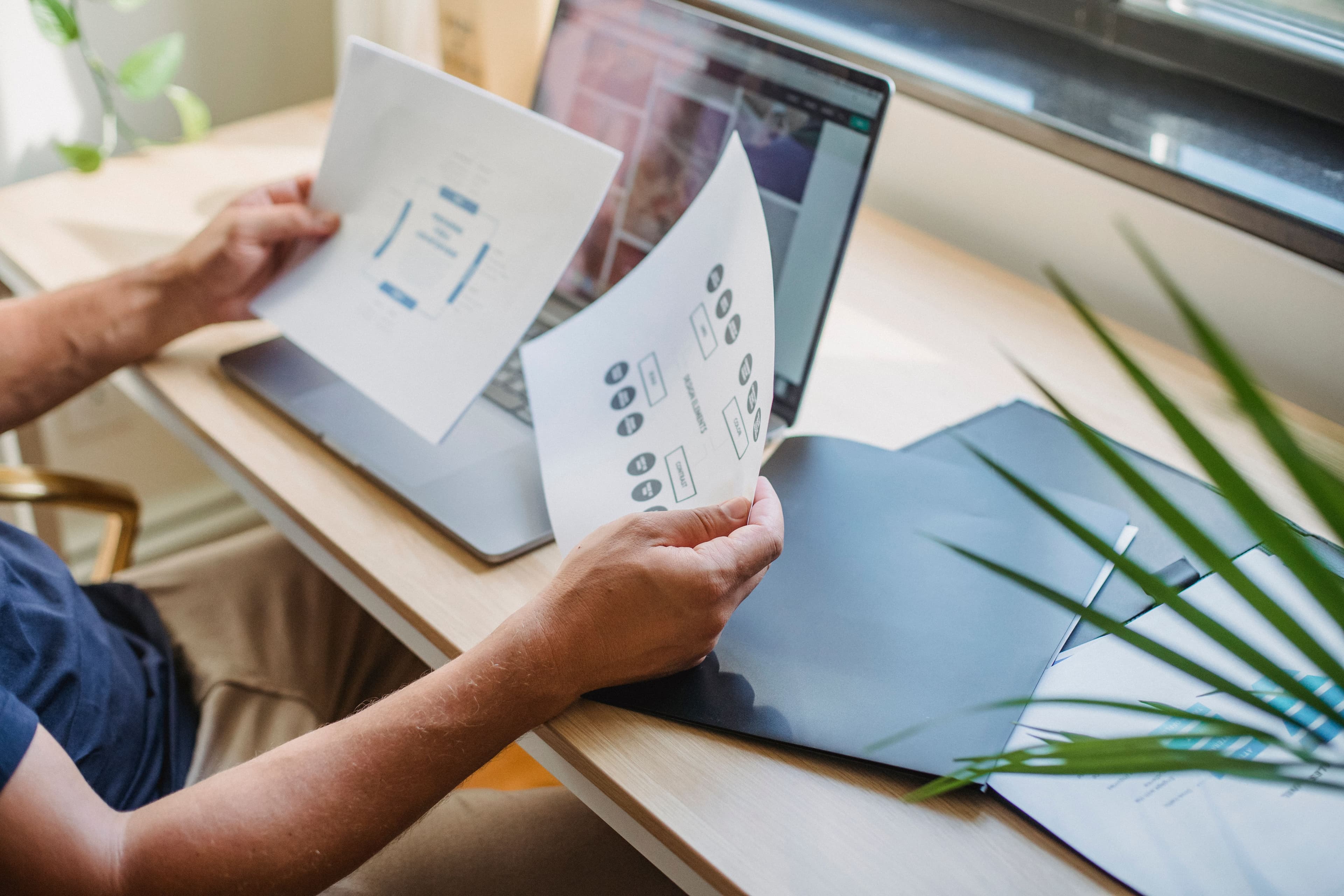 A person comparing two printed documents at a laptop
