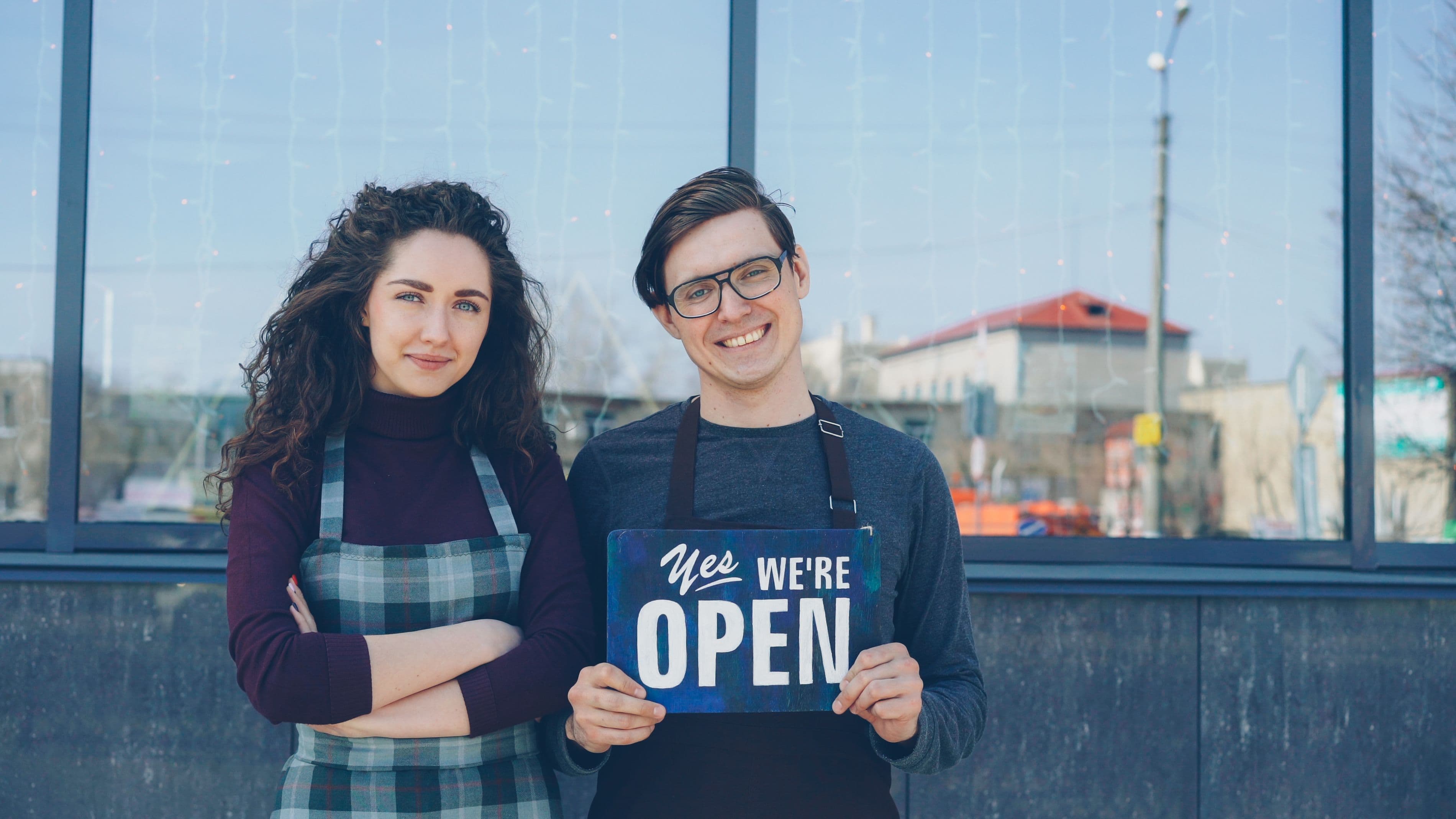 A couple in aprons holding an open sign outside their business