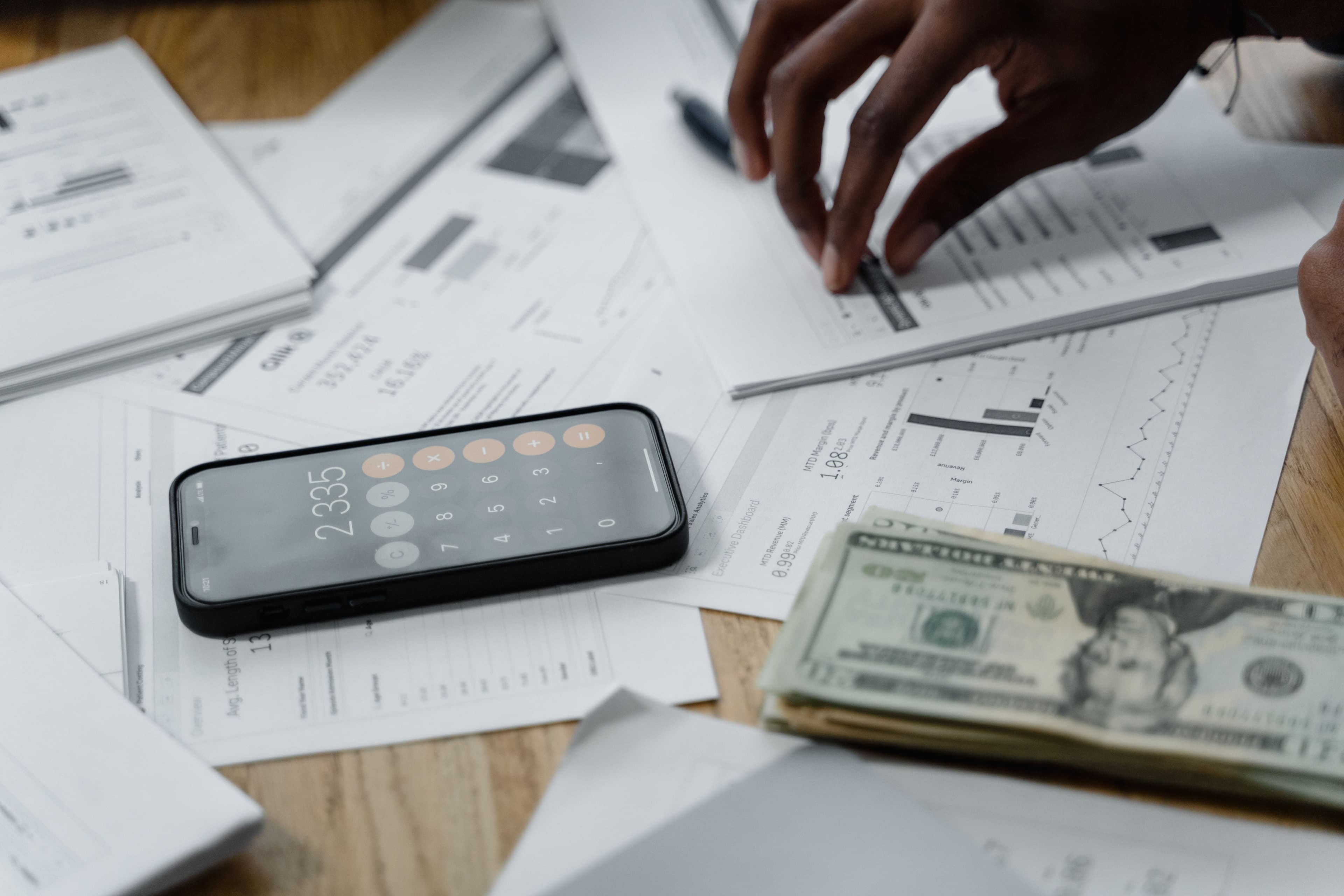 A phone calculator on financial reports beside a stack of cash